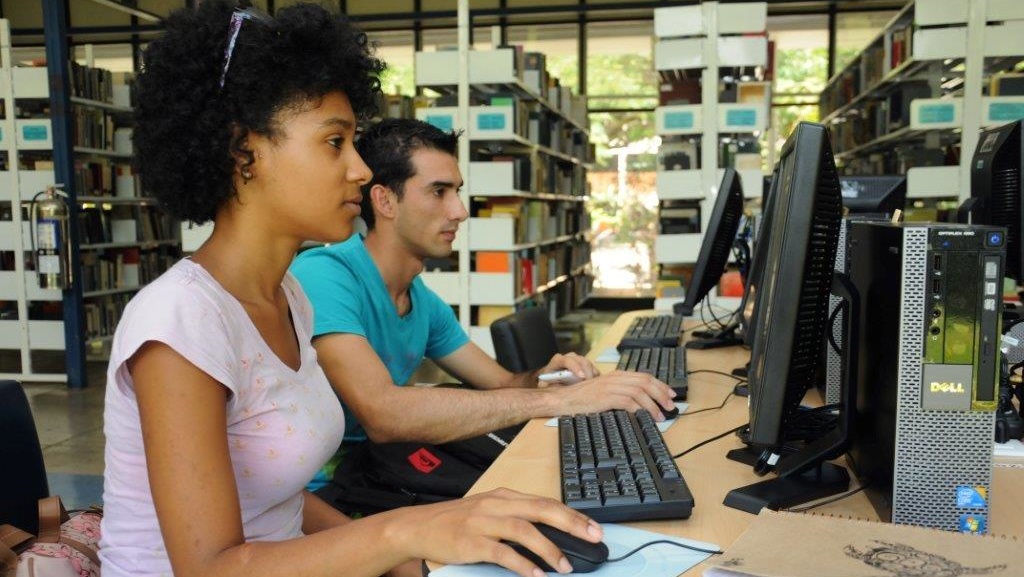 Jóvenes en estaciones de trabajo dentro de una biblioteca.