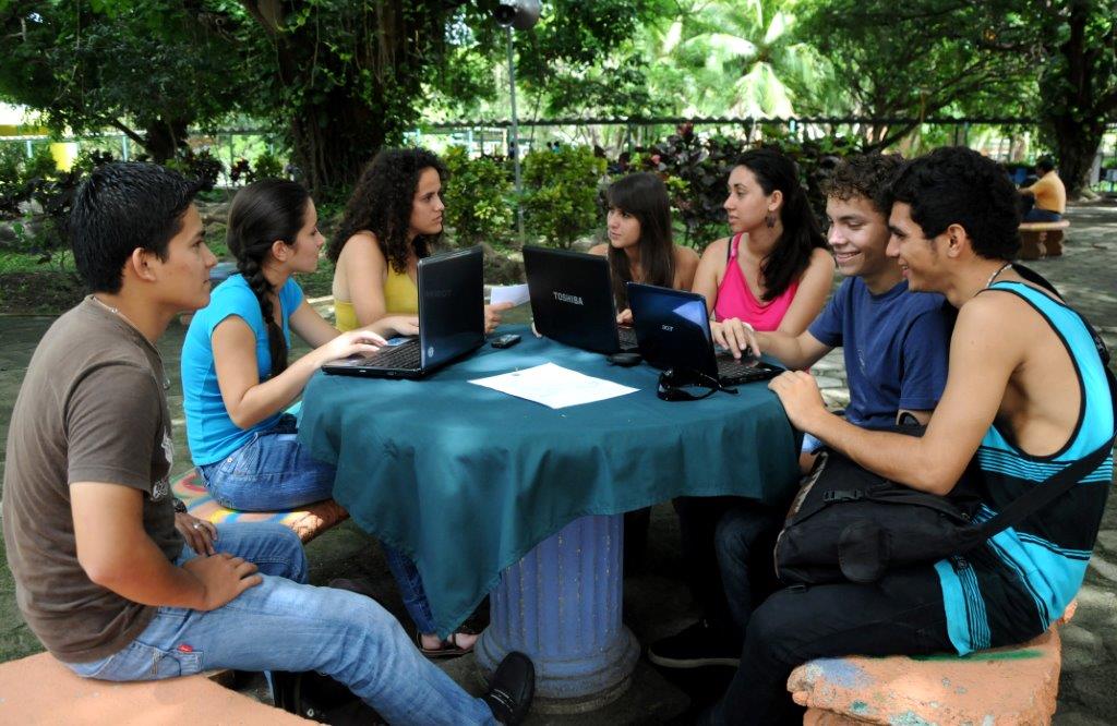 Grupo de jóvenes al aire libre estudiando en una mesa.
