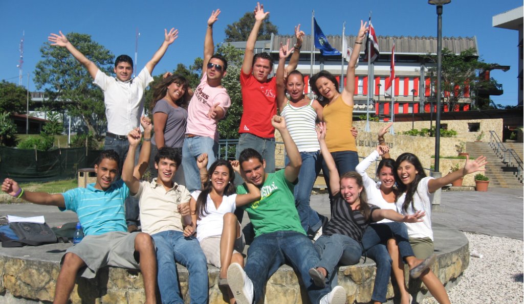 Grupo de jóvenes alegres levantando las manos, en un recinto educativo al aire libre